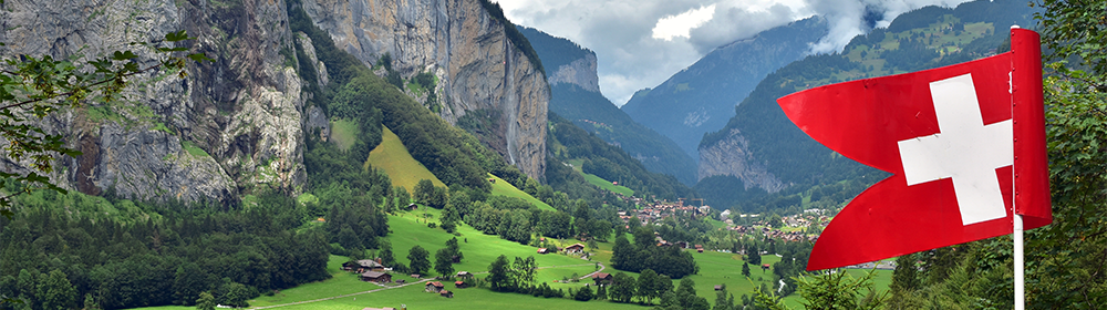 Panoramablick auf das Lauterbrunnental in den Schweizer Alpen mit alpinen Wiesen, Bergdorf und Schweizer Flagge im Vordergrund.