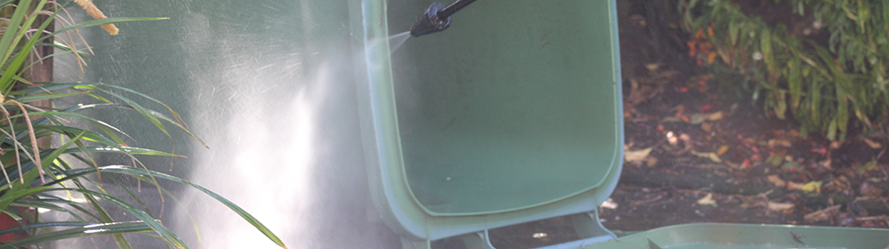 Grüne Mülltonne ist im Garten mit Hochdruckreiniger gründlich gereinigt